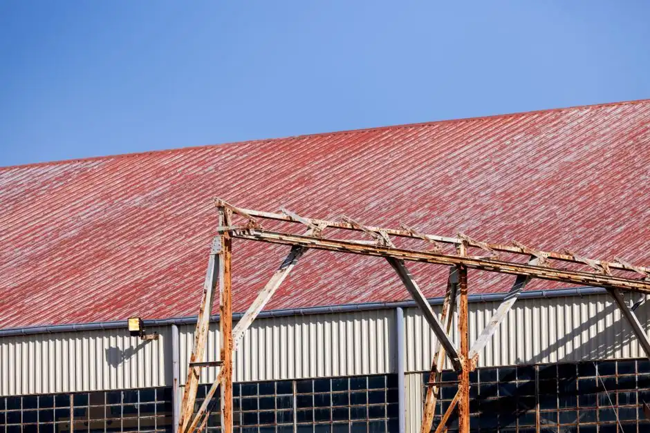 A weathered industrial warehouse with a rusted structure and red roof against a blue sky.