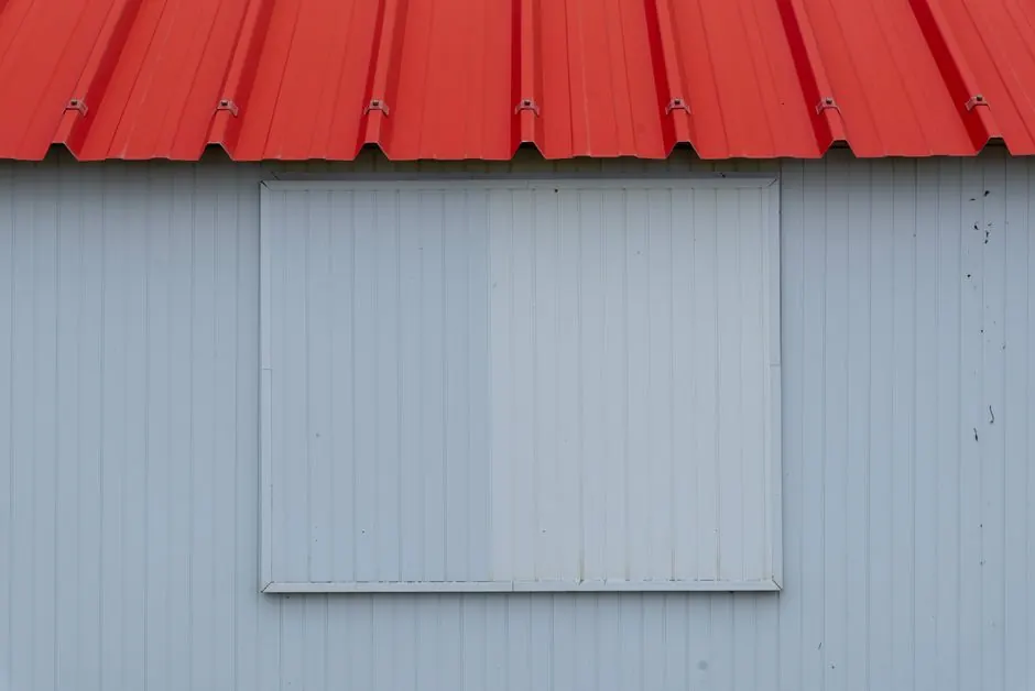 Minimalist image of a red metal roof with blue-grey corrugated panel wall.